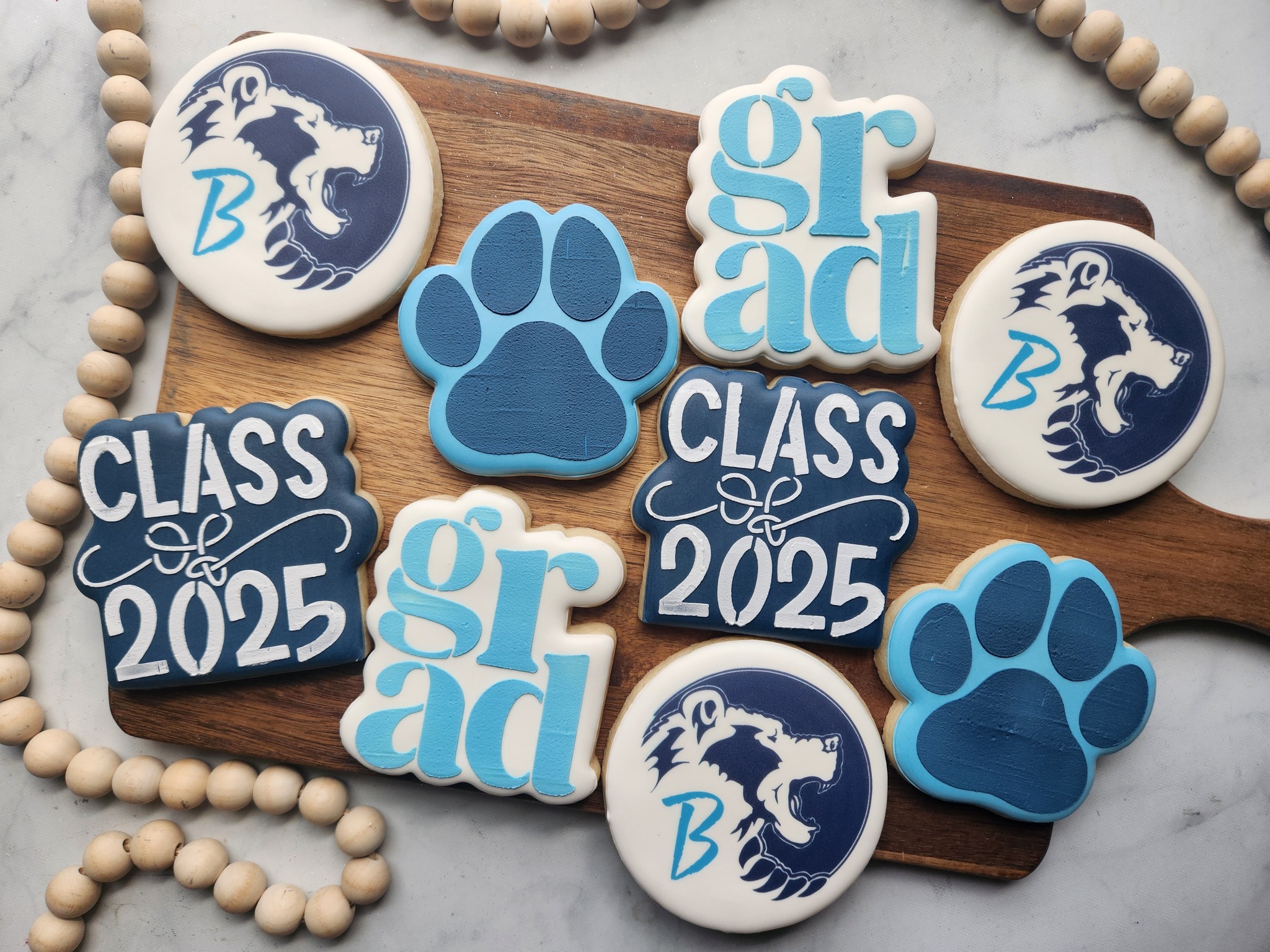 Blue and white graduation cookies with class year, school mascot, paw prints, and GRAD lettering