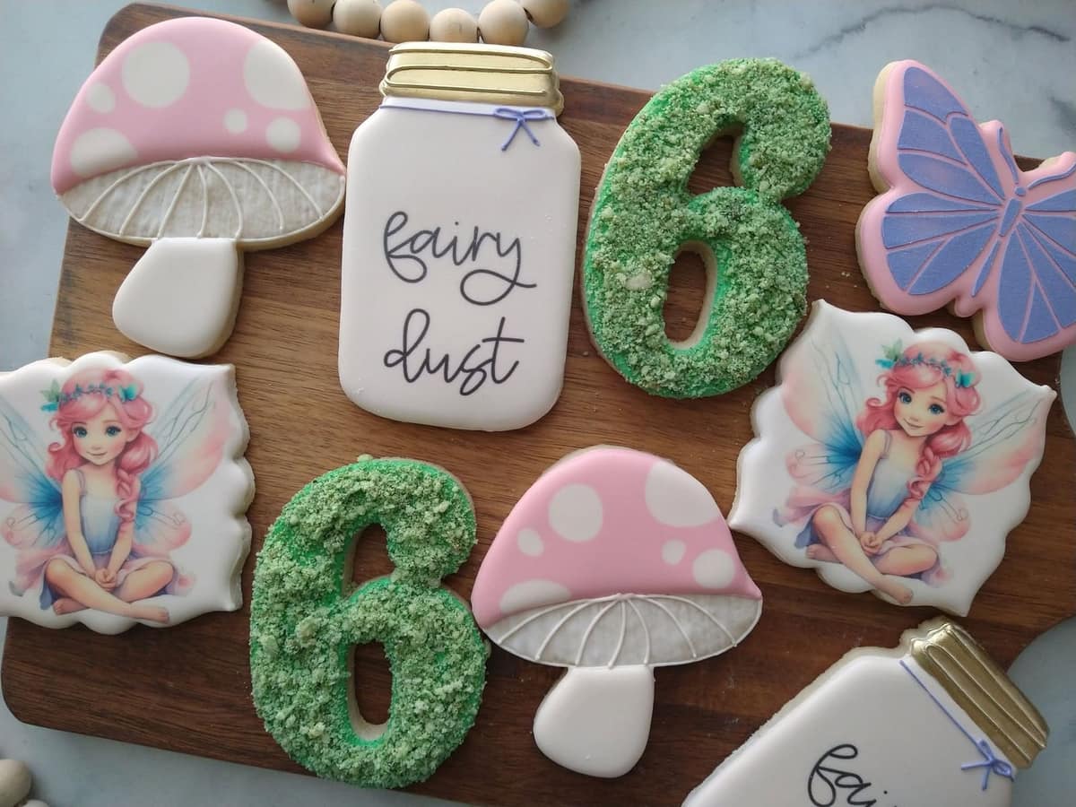 Fairy garden birthday cookies with pink mushrooms, a fairy dust jar, butterflies, fairies, and green number six cookies