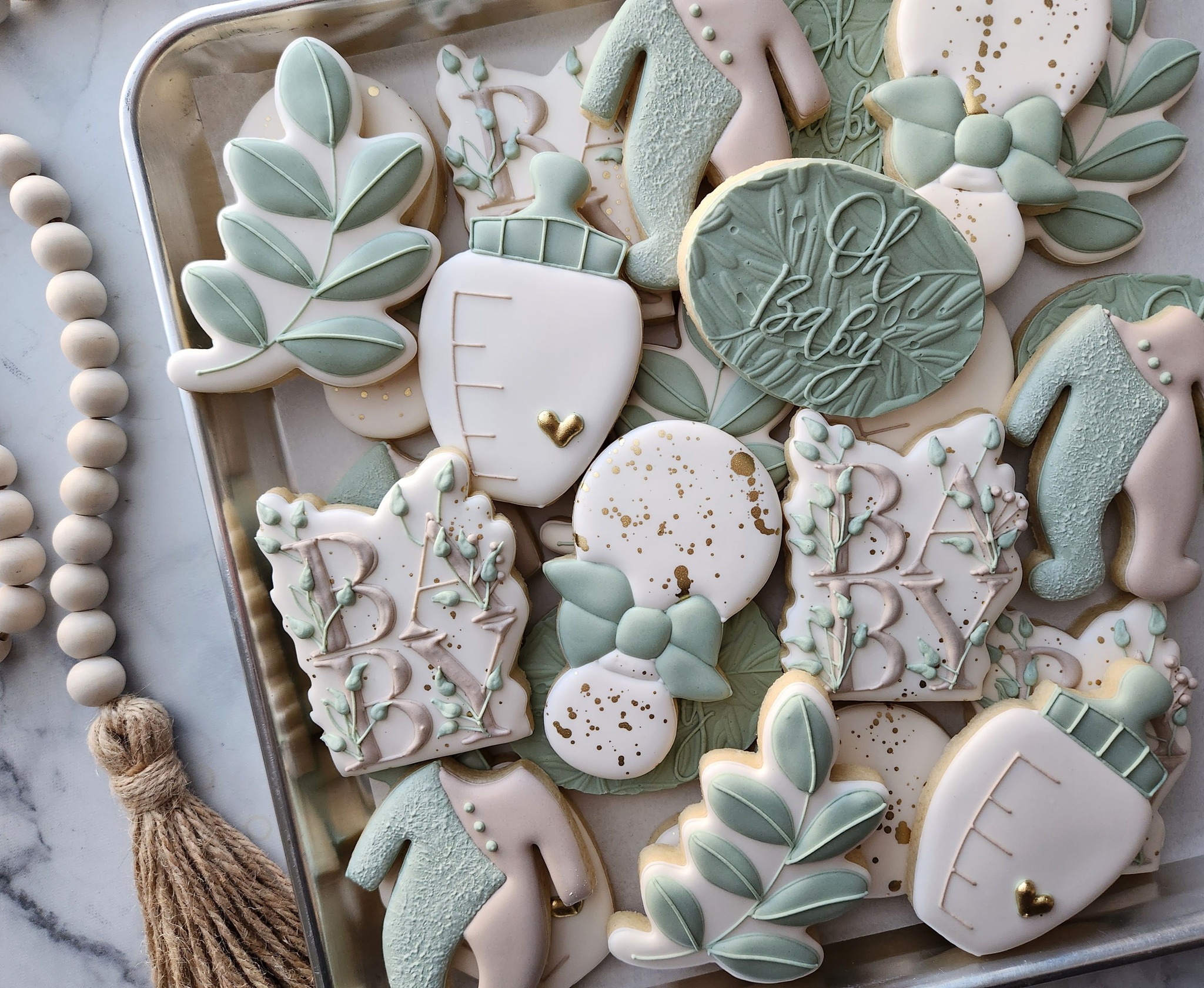 Sage and white baby shower cookies with bottles, baby clothes, leaves, bows, gold accents, and Oh Baby lettering